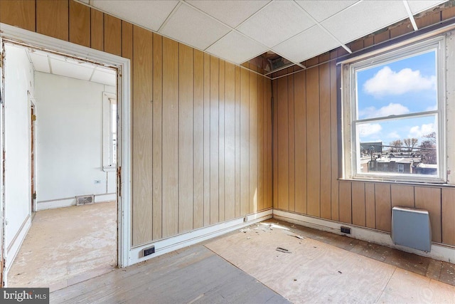 spare room featuring a drop ceiling, light wood-type flooring, and wood walls