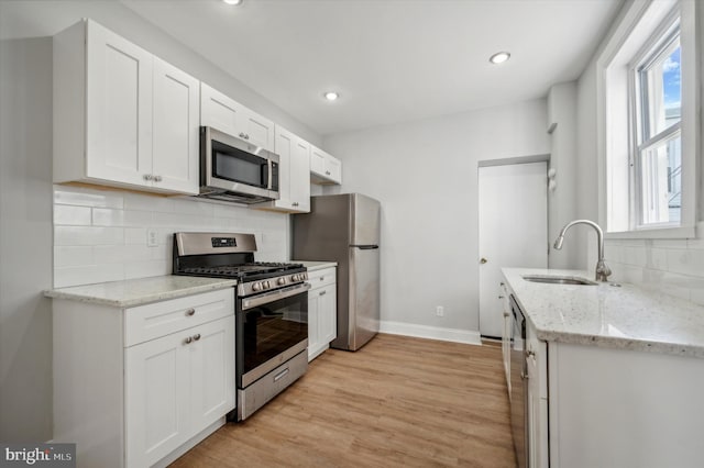 kitchen featuring white cabinetry, light stone countertops, light wood-type flooring, sink, and stainless steel appliances