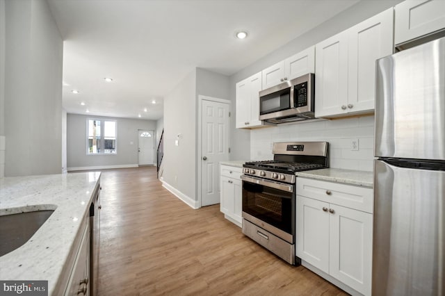 kitchen with white cabinetry, light stone counters, appliances with stainless steel finishes, and light hardwood / wood-style flooring