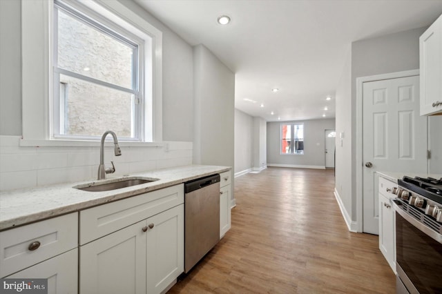 kitchen featuring white cabinets, light stone countertops, light hardwood / wood-style flooring, sink, and stainless steel appliances