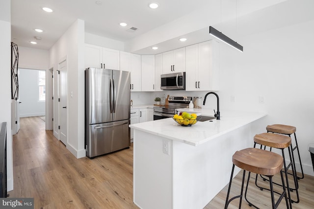 kitchen with appliances with stainless steel finishes, kitchen peninsula, light wood-type flooring, and white cabinetry