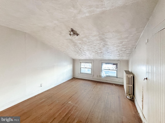 additional living space with radiator, lofted ceiling, wood-type flooring, and a textured ceiling