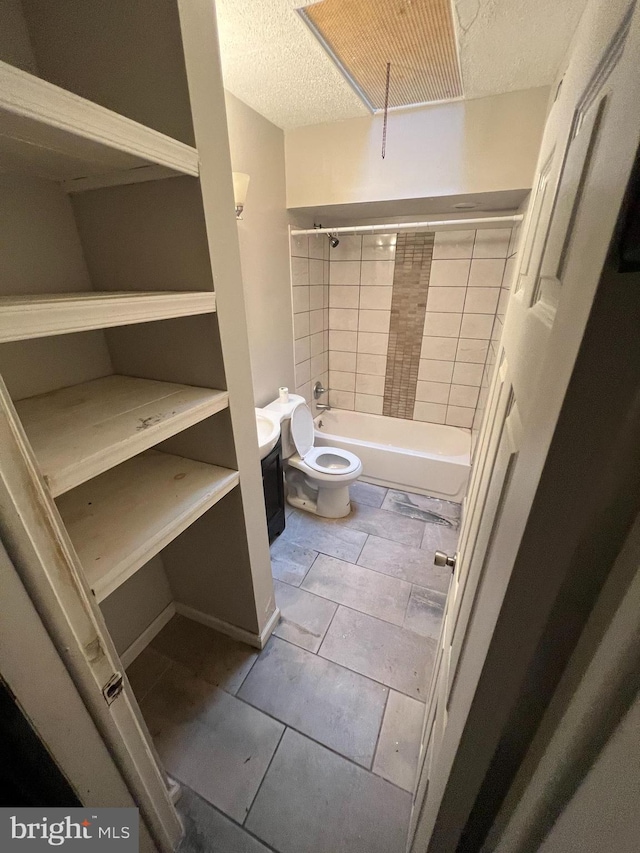 bathroom featuring tiled shower / bath, a textured ceiling, toilet, and tile patterned flooring