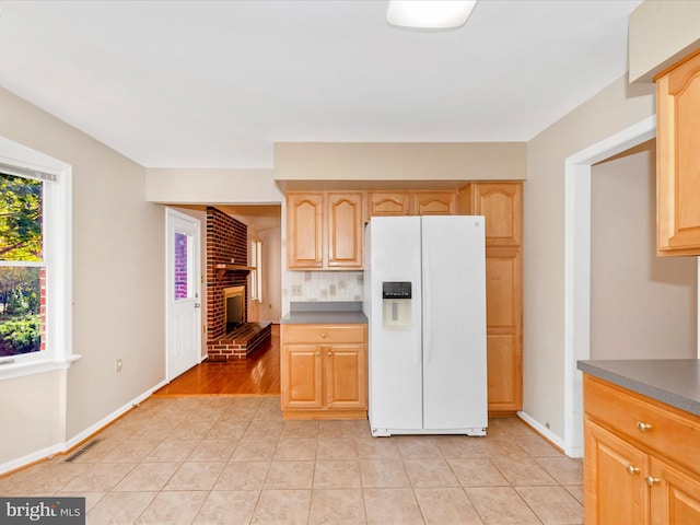 kitchen featuring light brown cabinets, backsplash, light tile patterned floors, a fireplace, and white refrigerator with ice dispenser