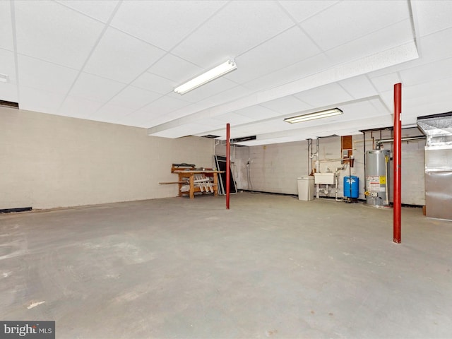 basement with a drop ceiling, water heater, and sink