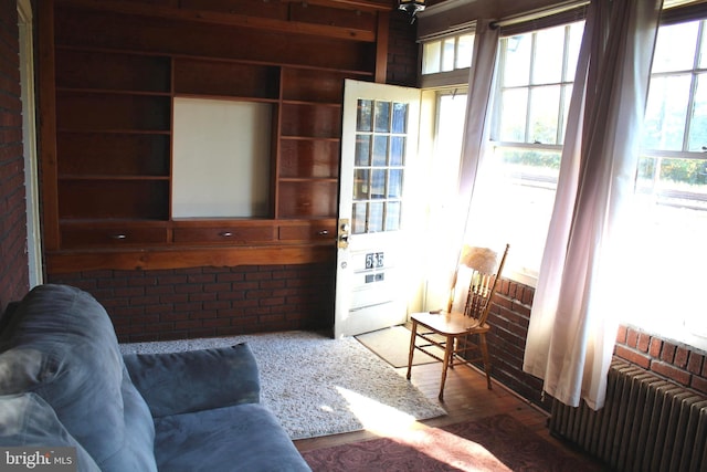 living room featuring radiator heating unit, dark wood-type flooring, and brick wall