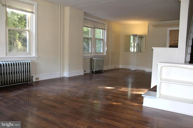 empty room featuring radiator heating unit, a healthy amount of sunlight, and dark hardwood / wood-style floors