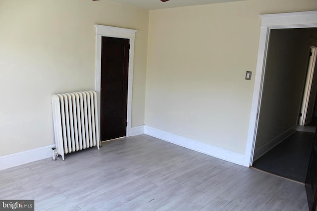 empty room featuring light wood-type flooring, radiator, and ceiling fan