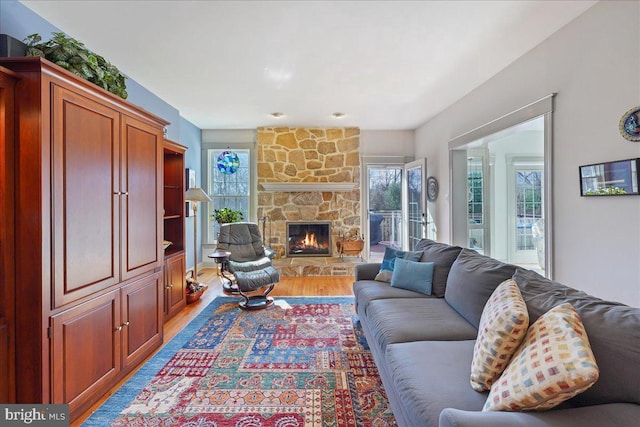 living room featuring plenty of natural light, a stone fireplace, and light hardwood / wood-style flooring