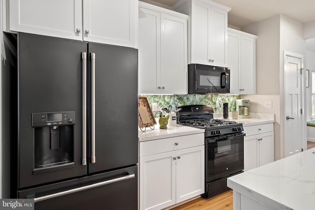 kitchen with black appliances, light stone countertops, white cabinetry, and light hardwood / wood-style flooring