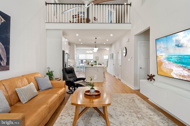 living room with light hardwood / wood-style flooring, a towering ceiling, and an inviting chandelier