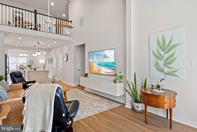 living room featuring a notable chandelier, light hardwood / wood-style floors, and a towering ceiling