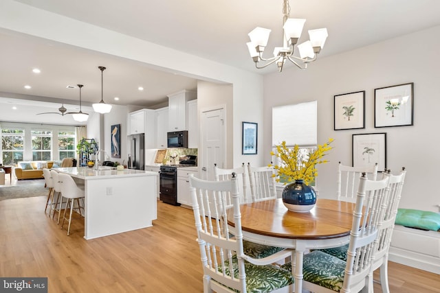 dining space featuring ceiling fan with notable chandelier, light hardwood / wood-style floors, and sink