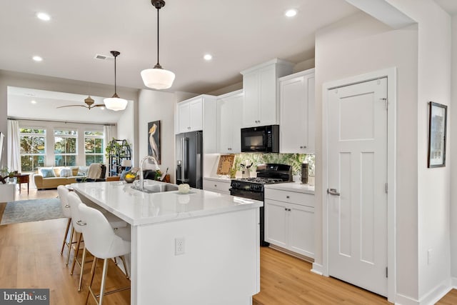 kitchen featuring a kitchen island with sink, black appliances, hanging light fixtures, light hardwood / wood-style flooring, and white cabinetry