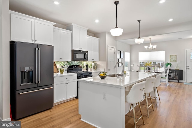 kitchen with white cabinetry, sink, decorative light fixtures, a center island with sink, and black appliances