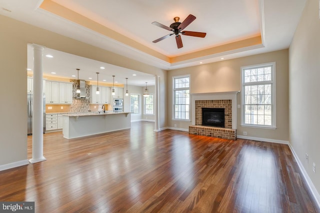 unfurnished living room with ceiling fan, a raised ceiling, wood-type flooring, and a fireplace