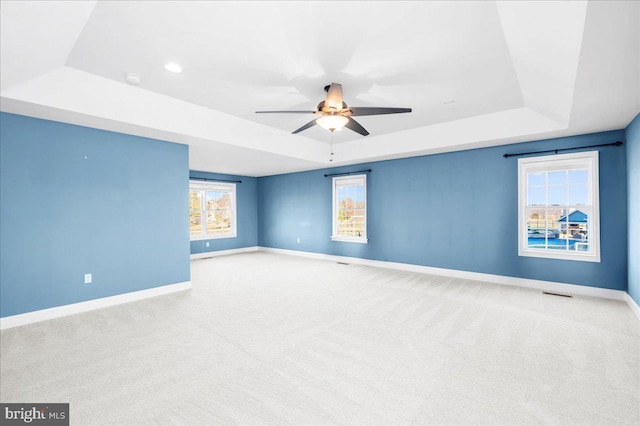 carpeted empty room with a tray ceiling, ceiling fan, and plenty of natural light