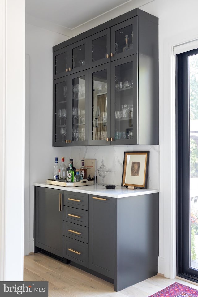 bar featuring backsplash, light hardwood / wood-style floors, and a healthy amount of sunlight