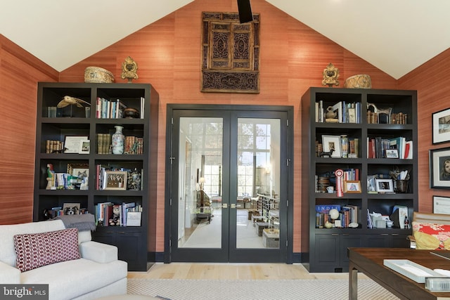 sitting room featuring french doors, light hardwood / wood-style floors, wood walls, and vaulted ceiling