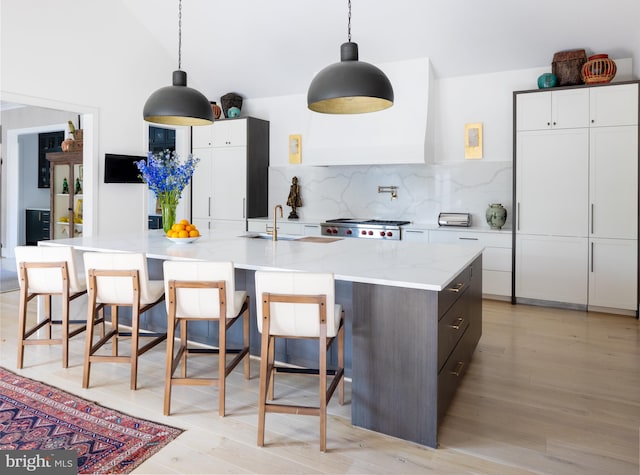 kitchen featuring white cabinetry, light wood-type flooring, hanging light fixtures, and an island with sink