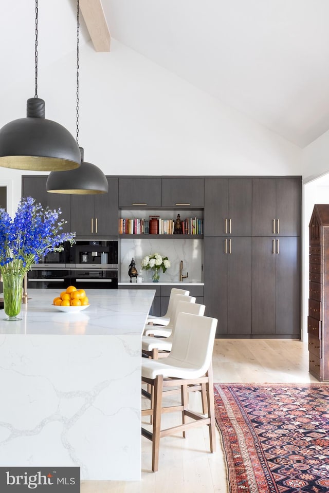 kitchen featuring pendant lighting, a breakfast bar area, light wood-type flooring, and high vaulted ceiling