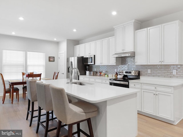 kitchen with light hardwood / wood-style flooring, stainless steel appliances, sink, and an island with sink