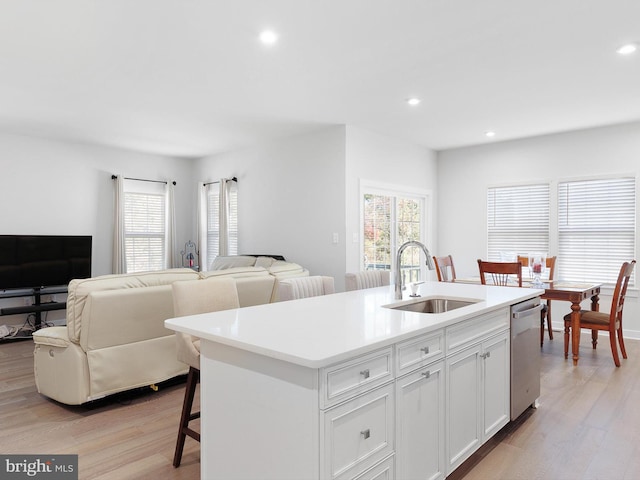 kitchen featuring dishwasher, sink, light hardwood / wood-style floors, white cabinets, and a kitchen island with sink