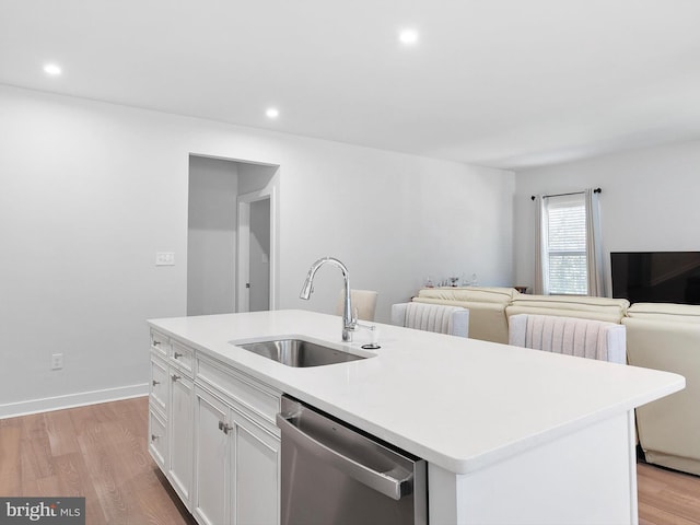 kitchen featuring white cabinets, an island with sink, stainless steel dishwasher, light hardwood / wood-style floors, and sink