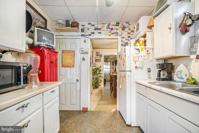 kitchen with a drop ceiling, white cabinets, sink, and white refrigerator