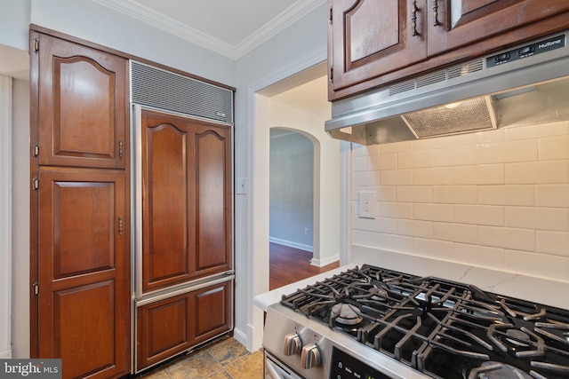 kitchen featuring paneled refrigerator, decorative backsplash, stainless steel gas stove, arched walkways, and under cabinet range hood