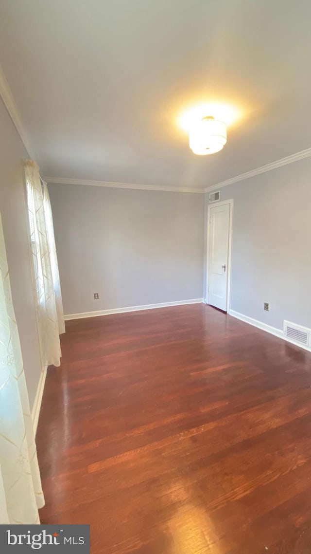 empty room with dark wood-style flooring, visible vents, crown molding, and baseboards