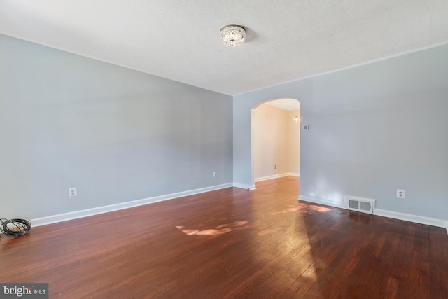 spare room featuring arched walkways, visible vents, hardwood / wood-style floors, and baseboards