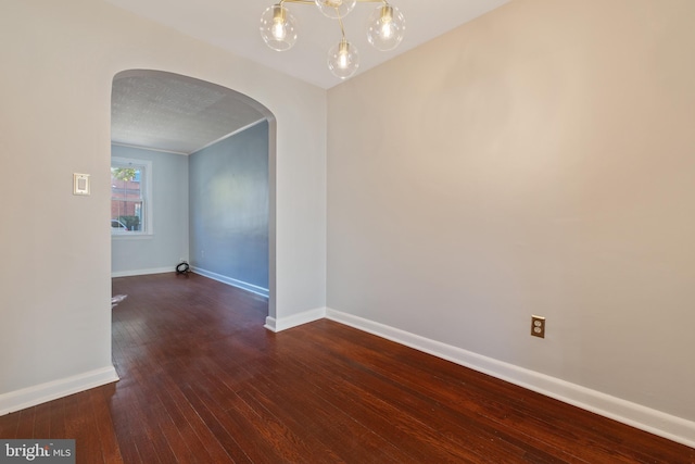 spare room featuring baseboards, arched walkways, and wood finished floors