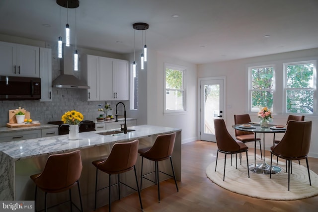 kitchen featuring light hardwood / wood-style floors, white cabinetry, hanging light fixtures, and a center island with sink