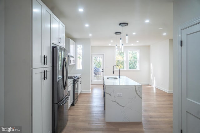 kitchen with a center island with sink, sink, white cabinets, decorative light fixtures, and appliances with stainless steel finishes