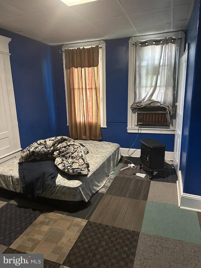 bedroom featuring a paneled ceiling, a wood stove, and dark carpet