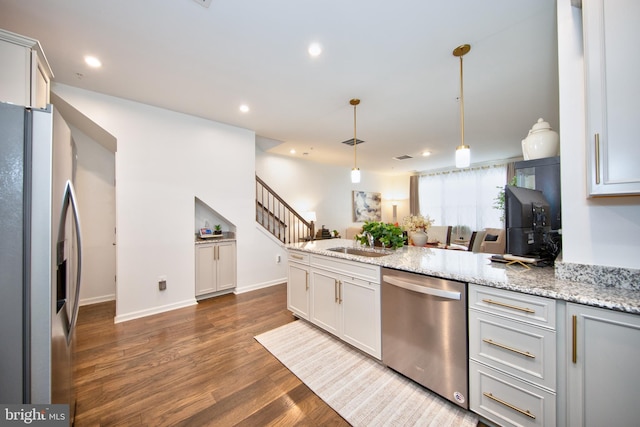 kitchen featuring dark wood-type flooring, stainless steel appliances, sink, decorative light fixtures, and light stone counters