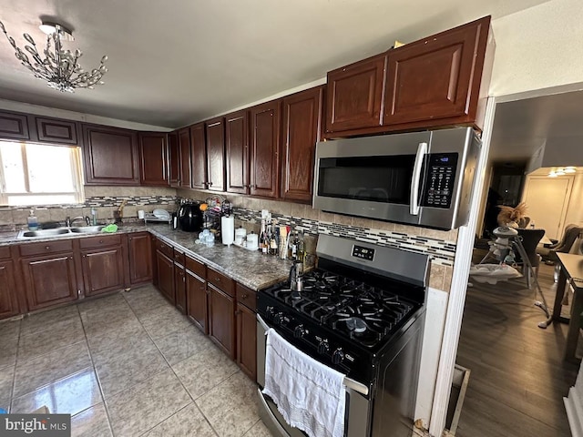 kitchen featuring sink, light tile patterned flooring, stainless steel appliances, decorative backsplash, and a chandelier