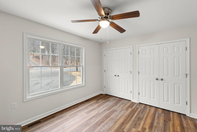 unfurnished bedroom featuring dark hardwood / wood-style flooring, two closets, and ceiling fan