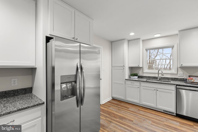 kitchen featuring dark stone counters, sink, light hardwood / wood-style flooring, appliances with stainless steel finishes, and white cabinetry