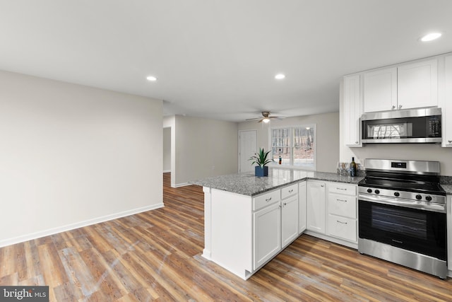 kitchen with kitchen peninsula, dark stone counters, stainless steel appliances, hardwood / wood-style flooring, and white cabinets