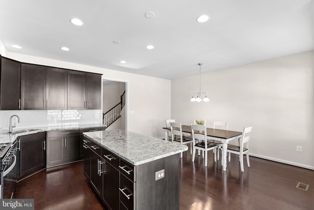 kitchen featuring sink, a center island, light stone counters, backsplash, and pendant lighting