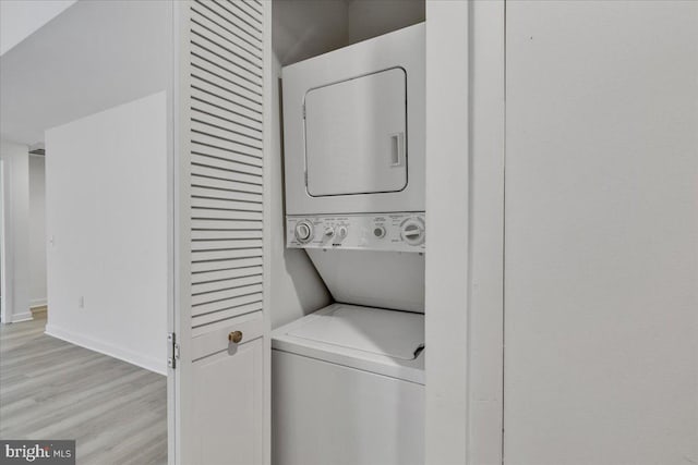 laundry room featuring stacked washing maching and dryer and light hardwood / wood-style flooring