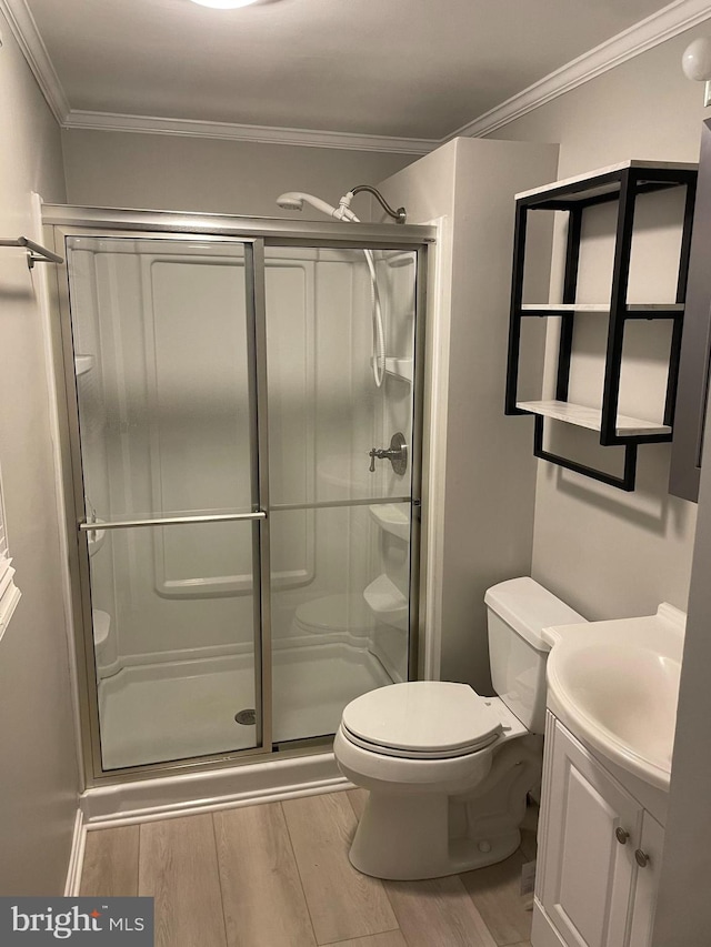 bathroom featuring wood-type flooring, toilet, ornamental molding, a shower with shower door, and vanity