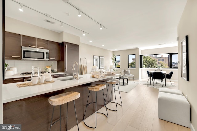 kitchen featuring sink, light wood-type flooring, backsplash, dark brown cabinets, and a kitchen breakfast bar