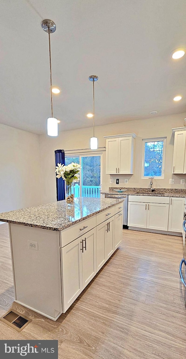 kitchen with light stone counters, a center island, white cabinetry, light wood-type flooring, and decorative light fixtures