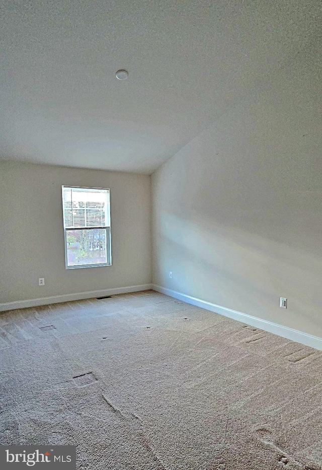 unfurnished room featuring a textured ceiling, light carpet, and vaulted ceiling