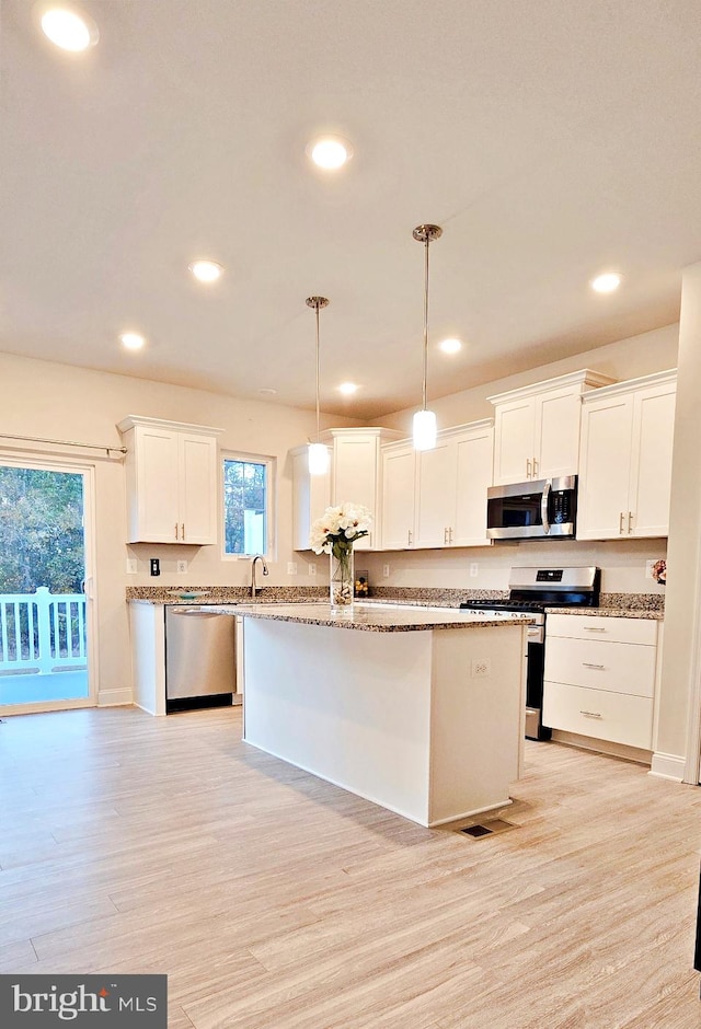 kitchen featuring a kitchen island, white cabinets, decorative light fixtures, and stainless steel appliances