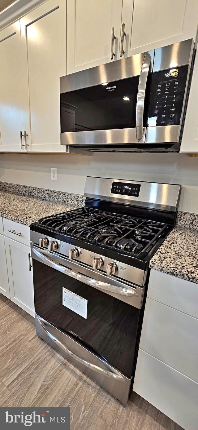 kitchen with white cabinetry, light wood-type flooring, appliances with stainless steel finishes, and light stone counters