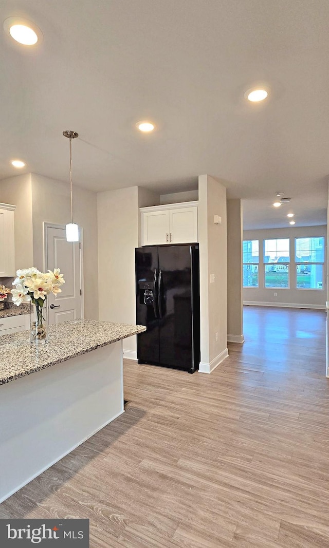 kitchen with decorative light fixtures, black fridge with ice dispenser, light stone countertops, white cabinets, and light hardwood / wood-style flooring